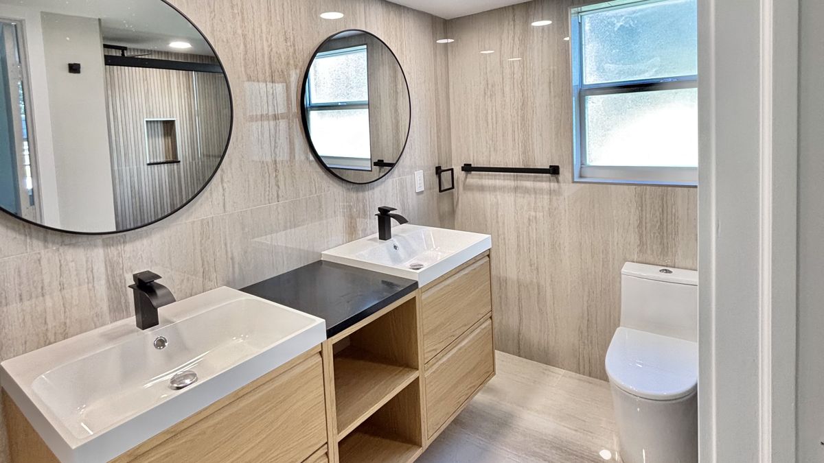 Remodeled bathroom with double floating wood vanity, round mirrors and stone-look tile, 3960 Oaks Clubhouse Dr #401, Pompano Beach